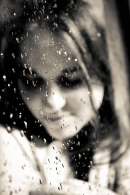 Güneşin yağmurlu bir pencere arkasında gülümseyen genç kız. Güneşin pencerenin yağmurdan sonra su damlaları ile genç kız. Vintage, grunge, eski, retro tarzı fotoğraf.