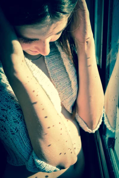 Young girl smiling behind a rainy window in the sun. Young girl in the sun by the window with drops of water after the rain. Vintage, grunge, old, retro style photo.