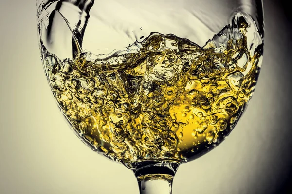 Stream of white wine pouring into a glass, white wine splash close-up on a grey background. Black and white photo with color of wine. Vintage, grunge, old, retro style.