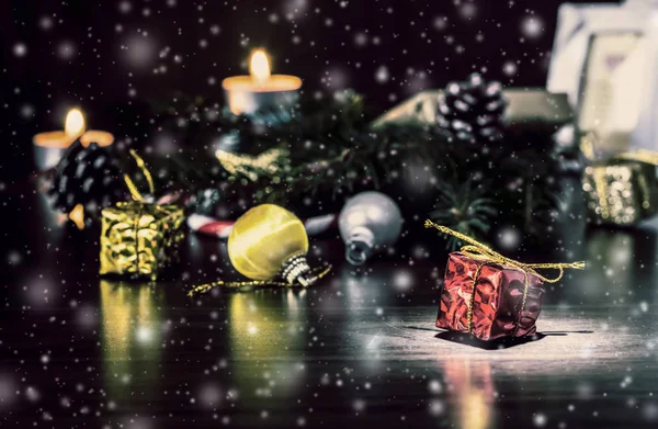 新年礼物在一个木质的古董桌上 在一个背景下 燃烧的蜡烛 圣诞树与锥和美丽的飘落的雪 圣诞节假期仍然生活与美丽的下降雪 — 图库照片
