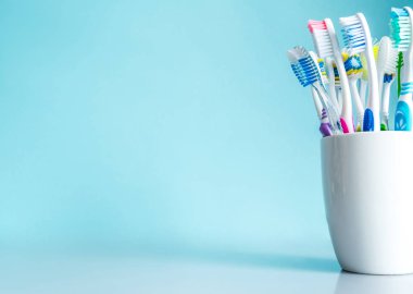 Banyoda ayna tablo üzerinde mavi bir arka plan üzerinde beyaz kupa yakın çekim olarak çok renkli diş fırçaları.