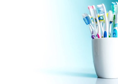 Multi-colored toothbrushes in a white mug close-up with a gradient background from white to blue with an isolated place for text