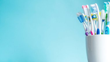 Banyoda ayna tablo üzerinde mavi bir arka plan üzerinde beyaz kupa yakın çekim olarak çok renkli diş fırçaları.