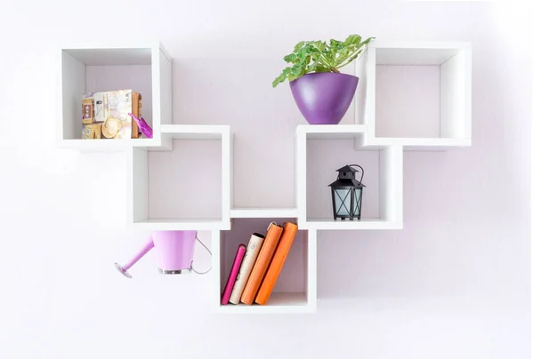 A modern white bookshelf on a white wall with a few things and a flower. Minimalism style.