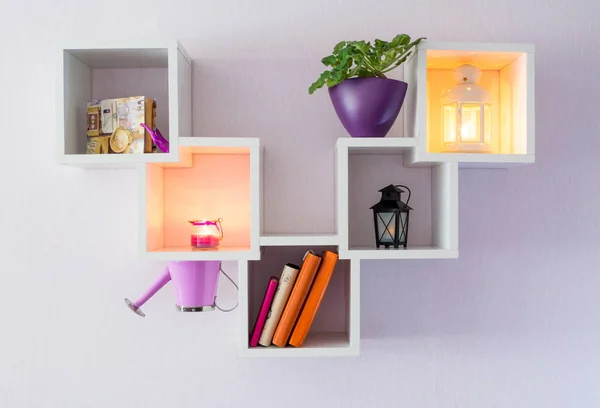 A modern white bookshelf on a white wall with a few things, a flower, and burning candles. Minimalism style.