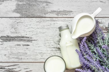 Vintage glass bottle with milk, a glass with milk and a beautiful white jug next to a branch of lavender flowers on a vintage wooden background. View from above. clipart