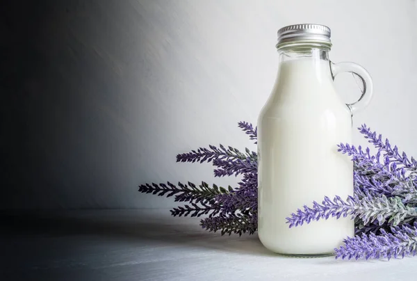 Vintage bottle with milk, near a branch of lavender flowers on a white vintage background