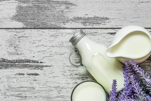 Vintage glass bottle with milk, a glass with milk and a beautiful white jug next to a branch of lavender flowers on a vintage wooden background. View from above.