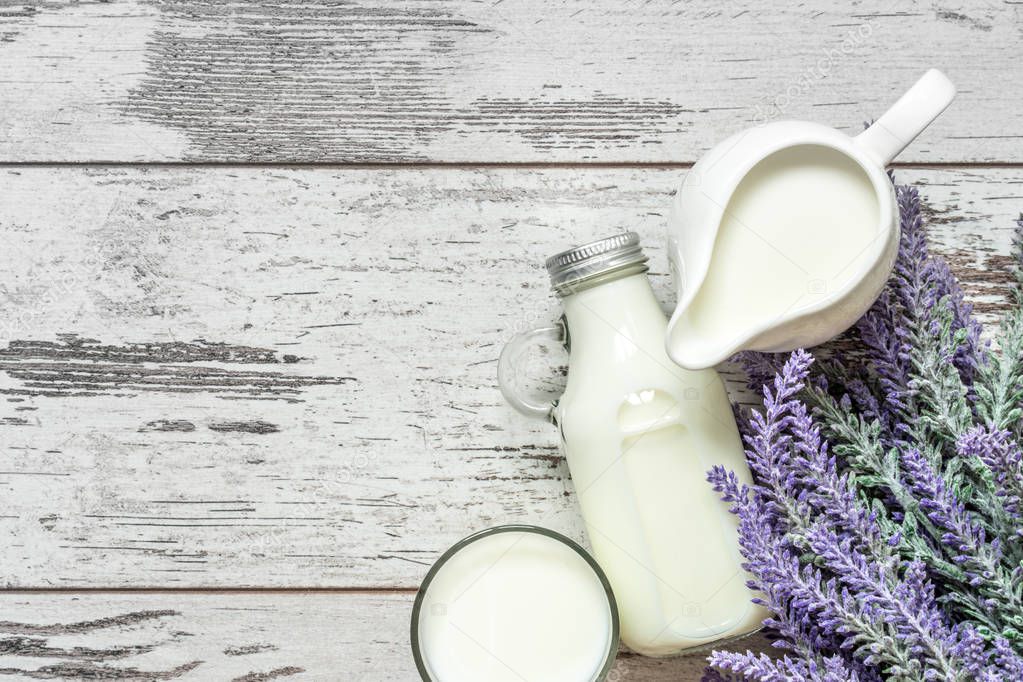 Vintage glass bottle with milk, a glass with milk and a beautiful white jug next to a branch of lavender flowers on a vintage wooden background. View from above.