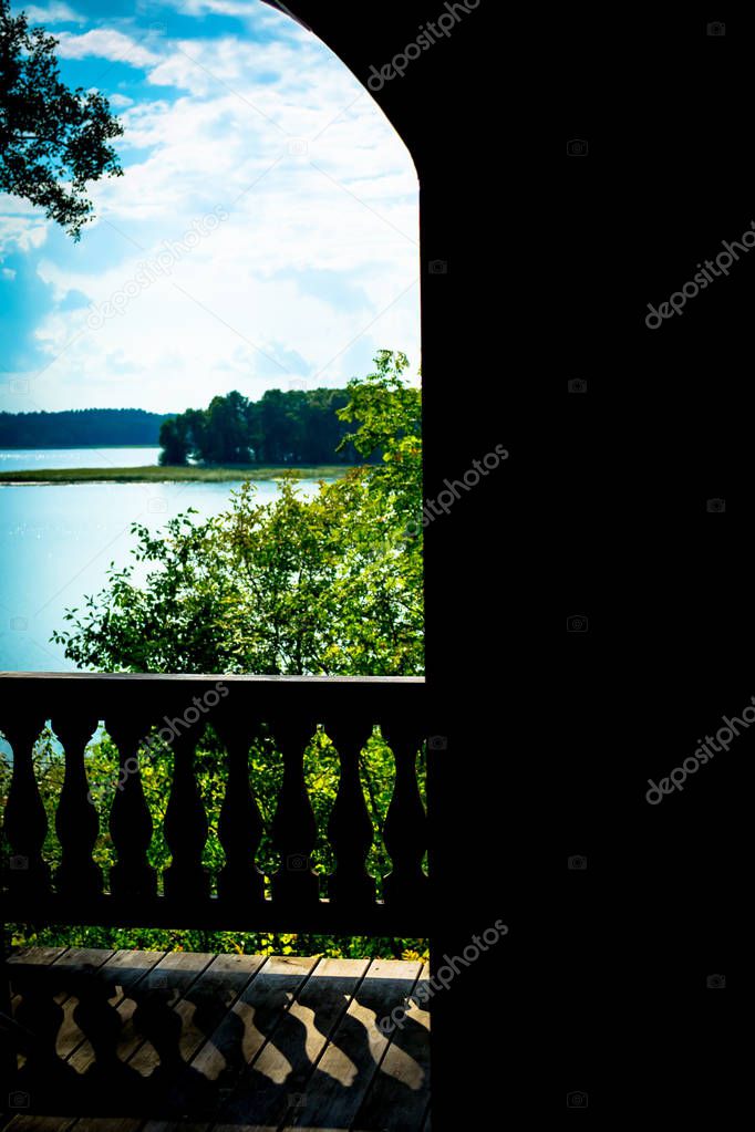 View of the forest landscape with a lake on a clear sunny day through the open door of a house with an ancient terrace.