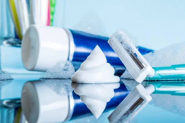 A regular disposable razor and shaving cream close-up in the foam in a modern bathroom on a glass reflective surface against a blue background.