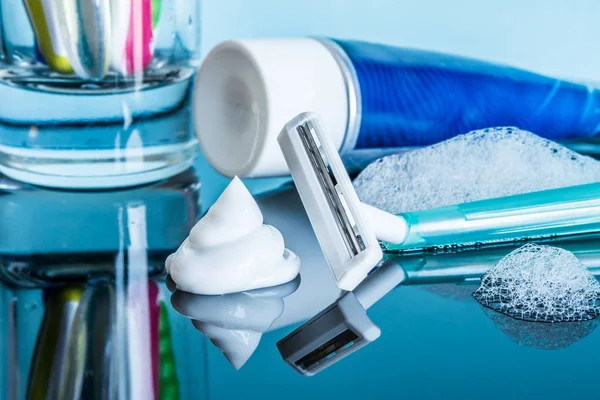 Una afeitadora desechable regular y crema de afeitar de cerca en la espuma en un baño moderno sobre una superficie reflectante de vidrio sobre un fondo azul . — Foto de Stock
