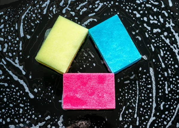 Esponjas coloridas con espuma de primer plano sobre un fondo de vidrio negro — Foto de Stock