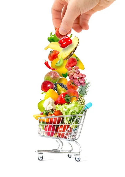 Lidská ruka, která dává hromadu čerstvého ovoce a zeleniny do přeplněné nákupní košíku izolované na bílém pozadí — Stock fotografie