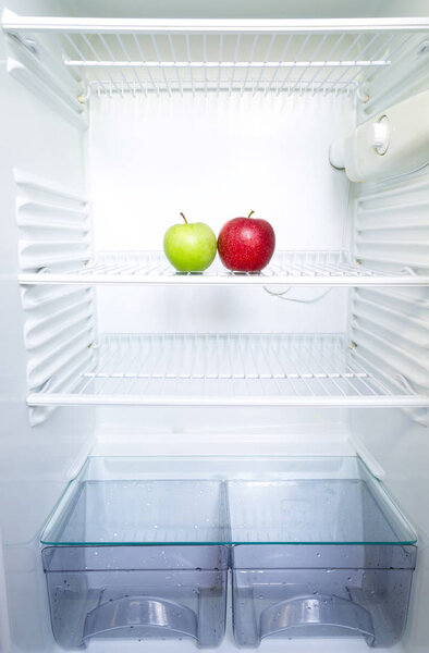 Bright fresh red and green apples on shelf of open empty refrigerator. Weight loss diet concept.