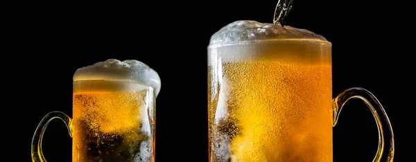 Dos grandes vasos de cerveza con espuma de cerca, uno frente al otro, aislados sobre un fondo negro. Dos vasos desbordantes de cerveza con espuma que fluye . —  Fotos de Stock