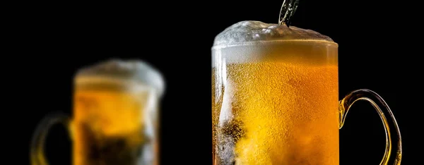 Two large glasses of beer with foam close-up, facing each other, isolated against a black background. Two overflowing glasses of beer with flowing foam.