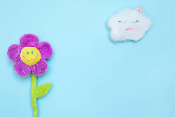 A funny cloud on a blue paper background and a toy flower with a smiling face. Photos on the theme of sunny summer weather