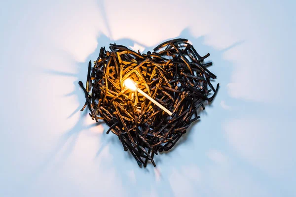 Heart symbol made of burned-down matches close-up with a burning match in the center and beautiful shadows. The concept of the complexity of love relationships, unhappy love. — Stock Photo, Image