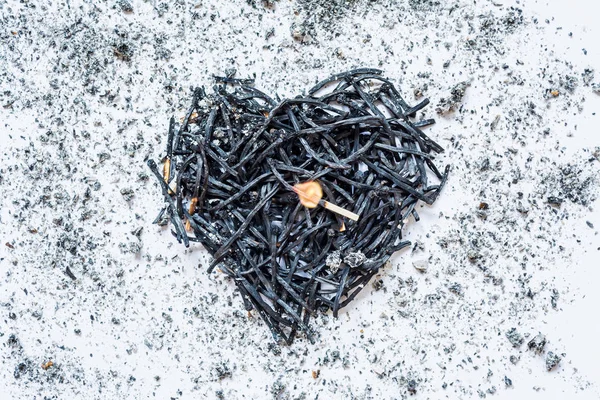 Heart symbol made of burned-down matches close-up with a burning match in the center and ashes around. The concept of the complexity of love relationships, unhappy love. — Stock Photo, Image