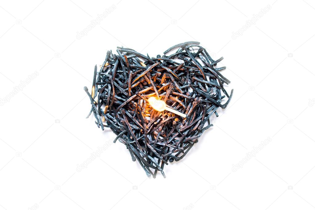 Heart symbol made of burned-down matches close-up with a burning match in the center, isolated on a white background. The concept of the complexity of love relationships, unhappy love.