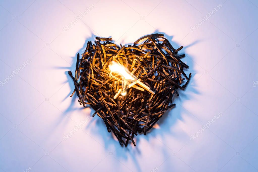 Heart symbol made of burned-down matches close-up with a burning match in the center and beautiful shadows. The concept of the complexity of love relationships, unhappy love.