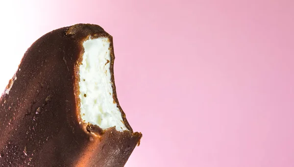 Bitten ice cream lolly in chocolate glaze close-up with condensate and icing frost on a soft pink background. Ice cream texture. — Stock Photo, Image