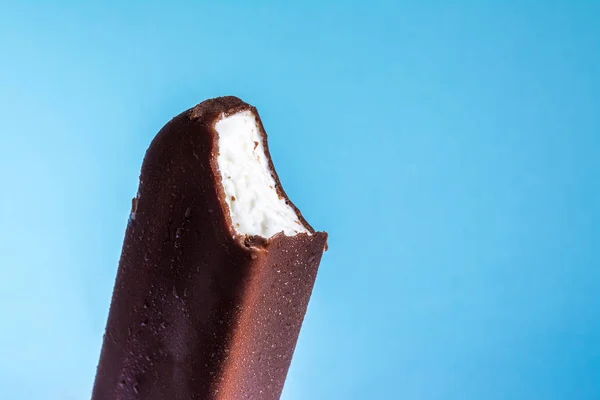Gelato morso lecca lecca in primo piano smalto di cioccolato con condensa e gelata glassa su uno sfondo cielo blu estivo. Texture gelato . — Foto Stock