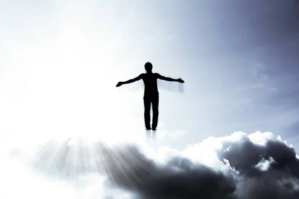 Silhueta de um homem voando no céu nos raios brilhantes do sol com os braços afastados . — Fotografia de Stock