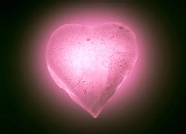 Cuore ghiacciato simbolo di colore rosa tenue primo piano incandescente al buio. Texture di ghiaccio con bolle . — Foto Stock