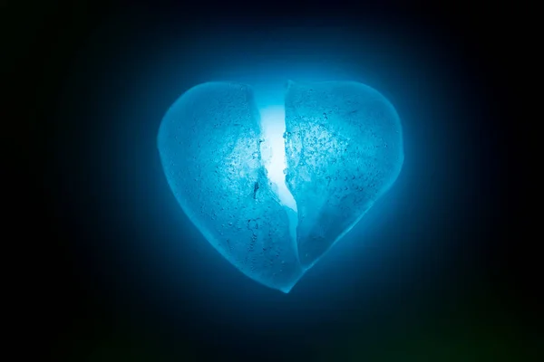 冰冻在半心脏符号的蓝色特写在蓝色冷光的黑暗中发光。冰块的纹理。破碎的心的象征。不幸的爱情的寓言. — 图库照片