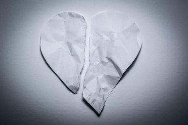 Eski, buruşuk kağıttan kalp sembolü, beyaz bir vintage arka plan üzerinde ikiye bölünmüş. Kırık bir kalbin sembolü, mutsuz aşk.
