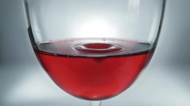 Kadehteki kırmızı şarap ve düşen şarabın yaratıcı makro yavaş çekim ham videosu. Yavaşça düşen şarap damlaları olan bir bardak..