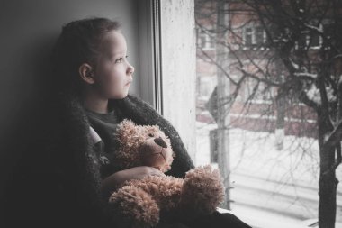 Bebek duygu. Küçük kız bir oyuncak ayı ile pencere kenarında oturur ve pencereden dışarı görünüyor. Çocuk Anne bekliyordum.