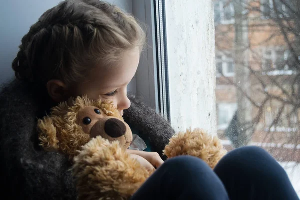 Bebek duygu. Küçük kız bir oyuncak ayı ile pencere kenarında oturur ve pencereden dışarı görünüyor. Çocuk Anne bekliyordum.