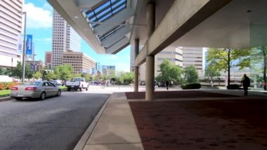 26 Eylül 2018. Baltimore, ABD. Kalabalık sokakta şehirde yürüyen insanlar. Yavaş hareket. Şehir siluetinin POV görünümü, gökdelenler ve Baltimore binaları. Şehir trafiği. Trafik geçen. 