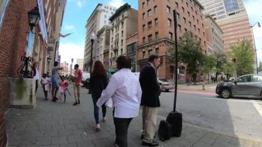 26 Eylül 2018. Baltimore, ABD. Kalabalık sokakta şehirde yürüyen insanlar. Yavaş hareket. Şehir siluetinin POV görünümü, gökdelenler ve Baltimore binaları. Şehir trafiği. Trafik geçen. 