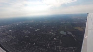 Uçak penceresi görünümü. Hava yolculuğu. Uçak pencere koltuğundan görünüm. Uçak uçuşundan yeşil manzara görünümü. Renkli gökyüzü ile bulutların üzerinde uçan bir uçağın kanadı. Uçak irtifa kazanıyor. Uçuş türbülansı. Yavaş Çekim.
