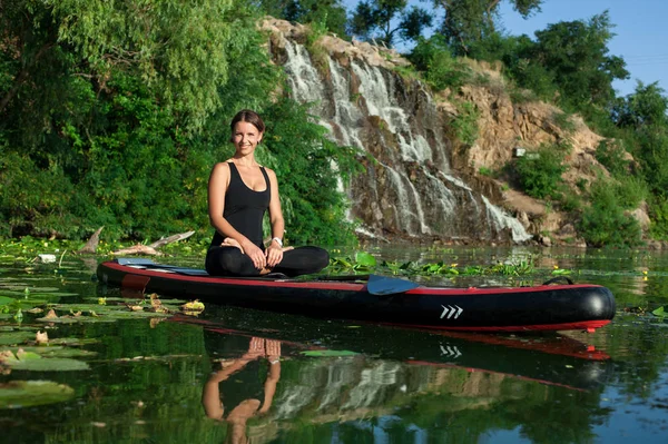 stand up paddle board yoga performed by beautiful girl on the bright city background, yoga training on the water