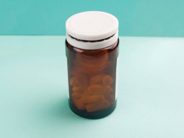 Turkuaz bir arka plan üzerinde beyaz kapsülleri ile şeffaf kahverengi plastik hapı şişe
