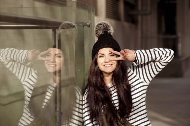 Mutlu kadın pon pon el barış işareti cam duvarının yakınında dururken eye yakınındaki ile şapkalı