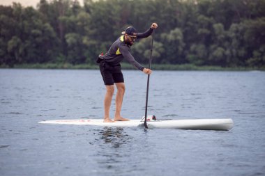 Sakallı atlet su sporları dahil. Kürek kürek nehir veya orman Gölü (paddleboard, Sup) tahtada ayağa eğitim süre ile ayakta genç adam