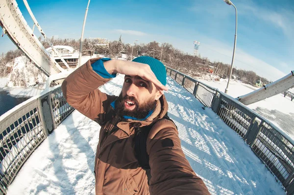 bearded guy is photographed against the sun, squints from the rays, stands on the bridge over the river