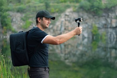 Gezgin holding Sabitleyici kamera çekimi fotoğraf süre için yan görünüm. Siyah T-shirt ve beyzbol şapkası takıyor