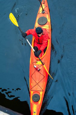 Kırmızı kayık koyu mavi su içerisinde yüzen kürekçi adamla üstten görünüm