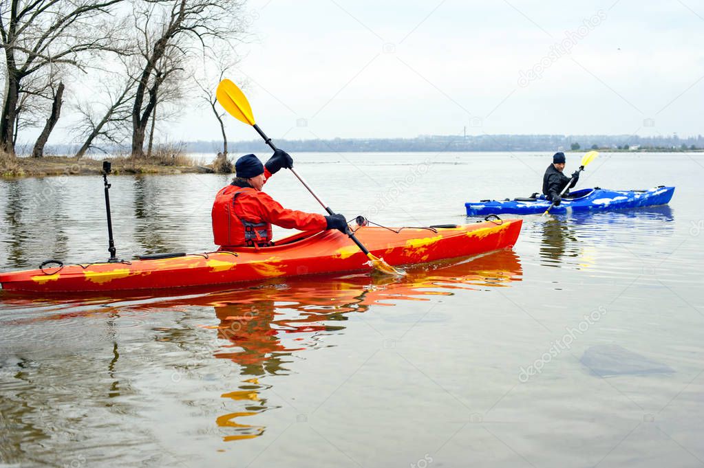 Canoeing competitions. Male athletes paddling a boat in quiet cold river in winter