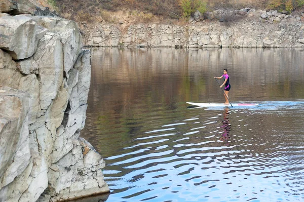 Levante-se paddle board fêmea cavaleiro em um lago entre praias rochosas — Fotografia de Stock