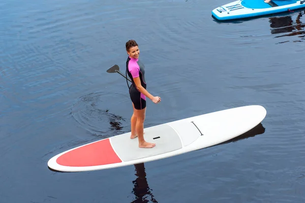 Fröhliche Frau paddelt auf Stand Up Board auf blauem Fluss — Stockfoto