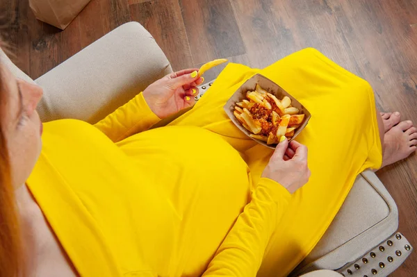 Mujer embarazada en vestido amarillo comiendo comida chatarra — Foto de Stock