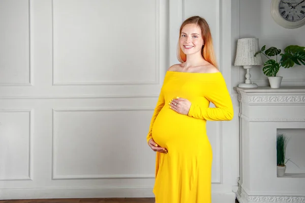 Sonriente señora embarazada brillante en vestido amarillo en casa —  Fotos de Stock